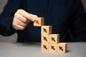 An image showing a man's hand placing wooden blocks with upward pointing arrows in order to symbolise why personal development is important